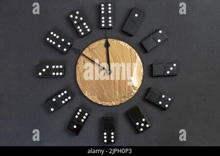 Beobachten Sie mit Domino-Figuren als Zahlen und einer goldenen Steinplatte in der Mitte, die 10 Minuten bis Mitternacht angezeigt wird Stockfoto