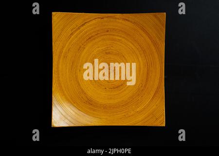 Quadratische Holzplatte mit konzentrischen Kreisen Muster. Orange strukturierte Schale isoliert auf schwarzem Hintergrund. Stockfoto