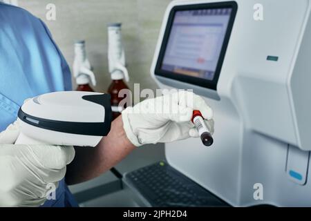 Scannen des Strichcodes des Reagenzglases mit Blut, Hämatologieanalysator auf Hintergrund, Nahaufnahme. Medizinisches Labor Stockfoto