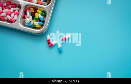 Mehrfarbige Kapseln in Edelstahlschale und auf blauem Hintergrund. Apothekenbanner. Pharmaindustrie. Pharmazie. Verschreibungspflichtiges Medikament Stockfoto