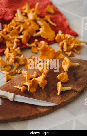 Frische Pfifferlinge auf einem hölzernen Schneidebrett mit einem Messer auf dem Küchentisch Draufsicht Stockfoto