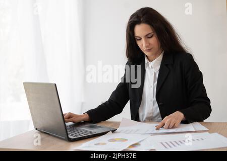 Seriöse Geschäftsfrau schreibt Dokumente auf einem Laptop, bereitet einen Bericht mit der Analyse der Ergebnisse Arbeit, Unternehmerin macht Papierkram an Stockfoto