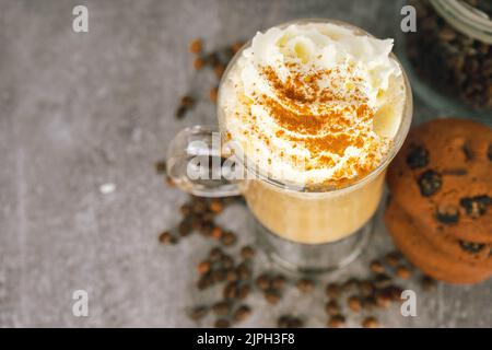 Eisgekühlter Karamell-Latte-Kaffee in einem hohen Glas mit Schlagsahne auf grauem Hintergrund und verstreuten Kaffeebohnen. Draufsicht, flach liegend mit Kopierplatz. Stockfoto