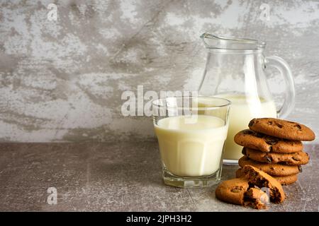 Glaskrug und Glas mit Milch und Schokoladenkekse auf grauem Hintergrund mit Kopierfläche. Stockfoto