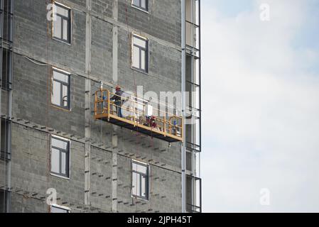 Der Baumeister arbeitet in einer speziellen Hängebühnbühne am Bau eines Mehrfamilienhauses Stockfoto