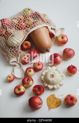 Herbsternte mit Sqush, Kürbis, roten Äpfeln in einem Mesh-Shopping-Öko-Beutel auf weißem Hintergrund. Kein Abfall, kein Kunststoffkonzept Stockfoto