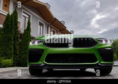 Modernes grünes Auto ist auf dem Parkplatz in der Nähe eines schönen Hauses mit Landschaftsgestaltung. Ansicht von unten. Stockfoto