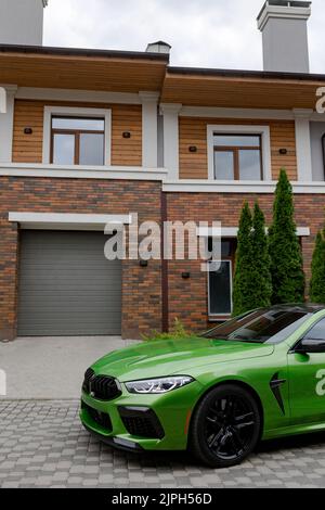 Modernes grünes Auto ist auf dem Parkplatz in der Nähe von Garagentor des schönen Hauses. Stockfoto