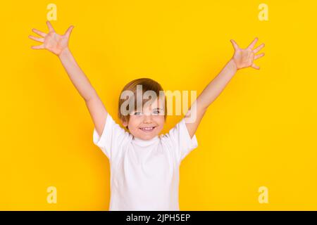 Portrait von attraktiven glücklich fröhlich Pre-teen Junge steigt Hände nach oben mit Spaß isoliert über hellen gelben Hintergrund Stockfoto