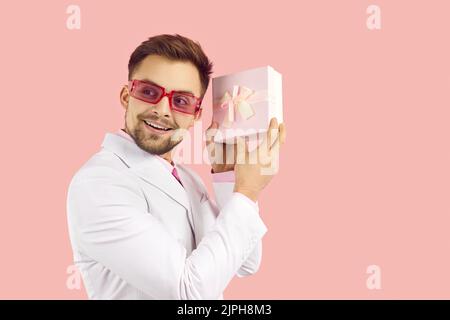 Glücklicher Mann isoliert auf rosa Hintergrund zitternd präsent und versucht zu erraten, was drin ist Stockfoto