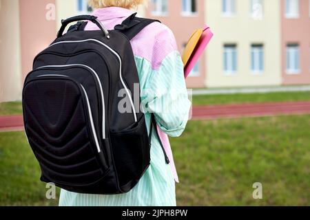 Schülerin mit schwarzem Rucksack und Heften für Notizbücher und Bücher in Händen gehen zur Schule Stockfoto