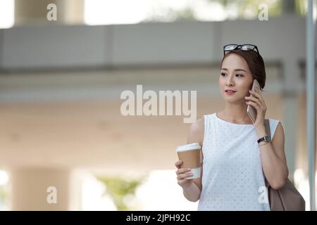 Schöne vietnamesische junge Frau mit Telefonanruf, wenn sie zur Arbeit eilt Stockfoto