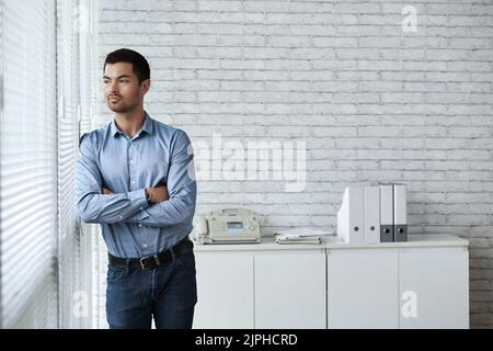 Hübscher junger Unternehmer, der am Bürofenster steht Stockfoto
