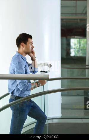 Junger Unternehmer mit einer Tasse Kaffee, der die Treppe hoch geht und am Telefon spricht Stockfoto