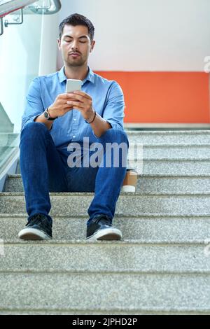 Hübscher junger Mann, der auf Treppen sitzt und Nachrichten auf dem Smartphone liest Stockfoto