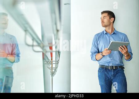 Betrachten Sie junge Unternehmer mit einem Tablet-Computer, der durch das Bürofenster schaut Stockfoto