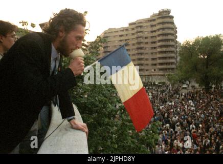 Bukarest, Rumänien, April 1990. „Golaniada“, ein großer Anti-Kommunismus-Protest auf dem Universitätsplatz nach der rumänischen Revolution von 1989. Die Menschen versammelten sich täglich, um gegen die Ex-Kommunisten zu protestieren, die nach der Revolution die Macht ergriffen hatten. Auf diesem Bild spricht der Anführer der Bewegung, Marian Munteanu, vom Balkon der Universität aus an die Menge. Stockfoto