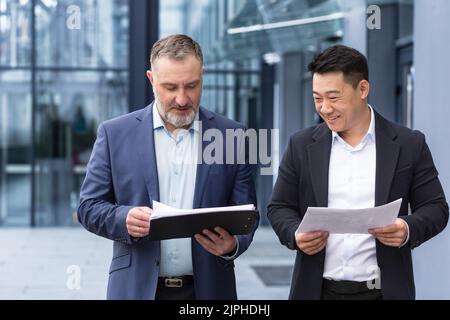 Verschiedene Gruppen von Geschäftsleuten, Männer, die über Pläne sprechen und diskutieren, Kollegen, die außerhalb des Bürogebäudes gehen, Arbeiter in Geschäftsanzügen Stockfoto