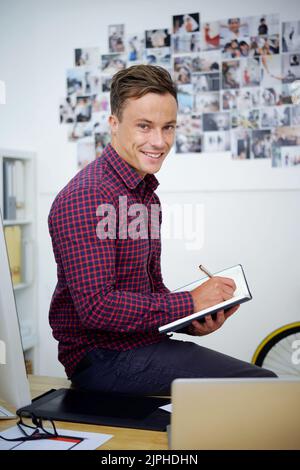 Lächelnder, gutaussehender Geschäftsmann, der sich Notizen in seinem Notizblock machte Stockfoto