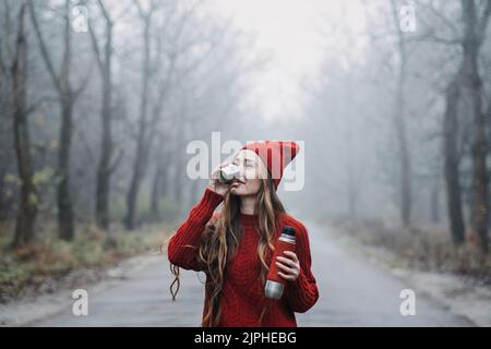 Allein junge Frau in rotem Hut mit Thermoskanne auf Naturhintergrund Stockfoto