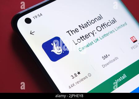 Die nationale Lotterie-App im Google Play Store auf dem Smartphone-Bildschirm auf rotem Hintergrund platziert gesehen. Nahaufnahme mit selektivem Fokus. Stafford, U Stockfoto