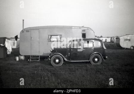 1950s, historisch, ein Auto aus einer früheren Ära, mit Speichenrädern, geparkt neben einem Wohnwagen auf einem Feld, einige Waschungen auf der Linie am Heck, England, Großbritannien. Stockfoto