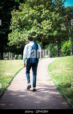 Der Geschäftsmann läuft im Park. Der junge Geschäftsmann schlendert mit seiner Jacke über seine Schulter. Stockfoto