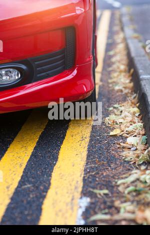 Rotes Auto auf gelben Linien mit Blättern geparkt Stockfoto