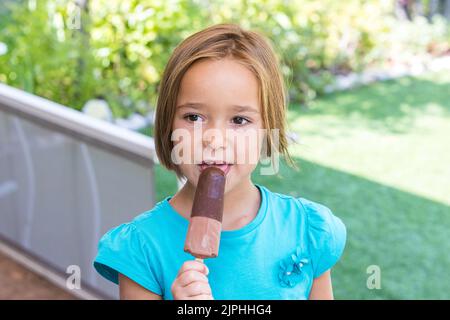 Mädchen in einem grünen T-Shirt, mit einem Milchschokoladeneis, auf der Straße, im Sommer. Eis, Eis, Eis, Essen, süß und Sommer-Konzept. Stockfoto