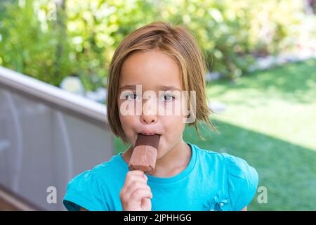 Mädchen in einem grünen T-Shirt, mit einem Milchschokoladeneis, auf der Straße, im Sommer. Eis, Eis, Eis, Essen, süß und Sommer-Konzept. Stockfoto