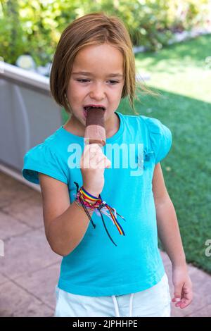 Mädchen in einem grünen T-Shirt, mit einem Milchschokoladeneis, auf der Straße, im Sommer. Eis, Eis, Eis, Essen, süß und Sommer-Konzept. Stockfoto