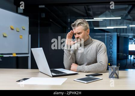 Erfahrene, grauhaarige Anleger, die in modernen Büros arbeiten, reifer Geschäftsmann, der über Entscheidungen nachdenkt, verärgert den Mann bei der Arbeit Stockfoto