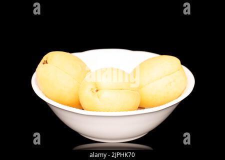 Drei leuchtend gelbe saftige Ananas-Aprikosen in einer Töpferei, Makro, isoliert auf einem schwarzen Hintergrund. Stockfoto