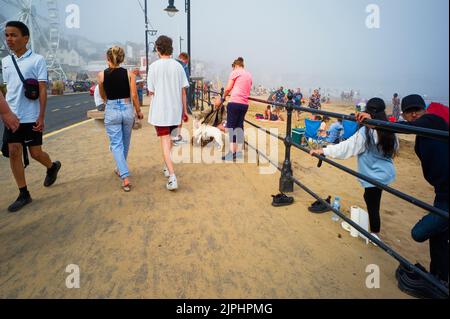 Geschäftige Szene an der Strandpromenade von Scarborough an einem nebligen Tag kommt der Sand direkt über den Bürgersteig Stockfoto