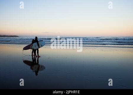 Surfpaar am Scarborough Beach in der Abenddämmerung mit Blick auf das Meer mit anderen Surfern in der Ferne Stockfoto