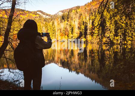 Nahaufnahme filmische Rückansicht kaukasische Frau Wanderer stehen am See Nehmen Sie Foto der malerischen Herbstnatur im Freien an sonnigen Tag im Freien. Berühmte Reise des Stockfoto