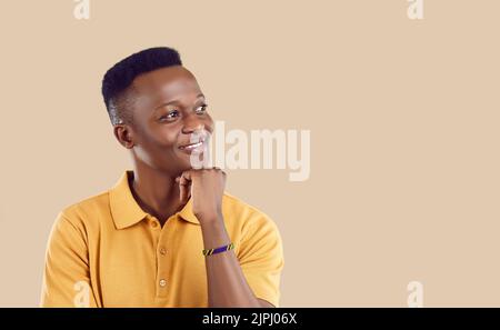 Der junge afroamerikanische Mann blickt weg mit lächelnden Requisiten, die mit der Hand von einer glücklichen Zukunft träumen Stockfoto