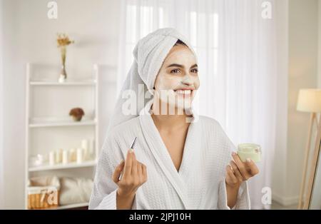 Portrait der schönen jungen Frau Anwendung kosmetische Gesichtsmaske während der morgendlichen Schönheitsroutine. Stockfoto