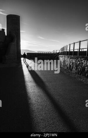Langer Schatten eines Mannes zu Fuß in Lyme Regis, Dorset Stockfoto