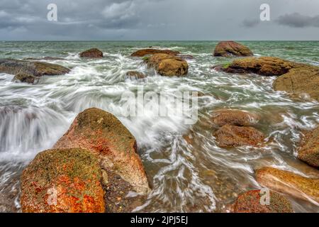 Eine Meereswelle bricht an Einem tropischen Strand gegen Einen bunten Sonnenuntergang Himmel Stockfoto