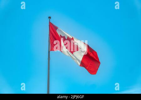 Eine große kanadische Flagge, die im Wind winkt, steht an einem Sommertag unter einem strahlend blauen Himmel Stockfoto