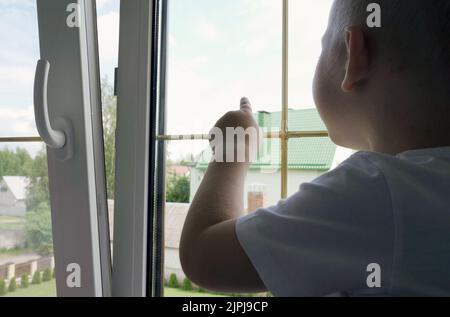 Ein kleiner Junge sitzt und schaut aus dem Fenster, zeigt mit dem Finger. Nahaufnahme Stockfoto