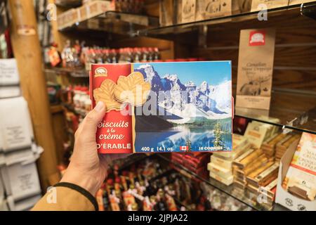 Banff, Alberta, Kanada - 6. Juli 2022: Hand hält eine Schachtel Ahornblatt-Cremekekse hoch, während sie in einem Geschenkeladen einkaufen Stockfoto