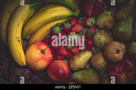Stillleben von Früchten auf einem Küchentisch, Banane, Apfel, Nektarine, schwarze Traube, Erdbeeren und Birnen, gesundes und veganes Essen Stockfoto