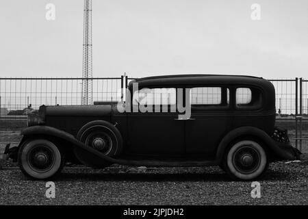 Eine Graustufenaufnahme eines Oldtimers auf dem Feld an einem Dock Stockfoto