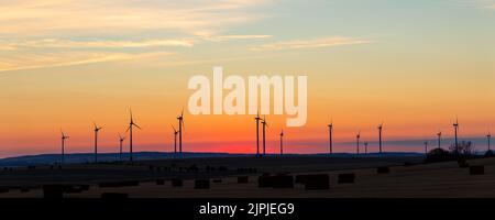 Panoramablick über die Landschaft, die neue moderne Windkraftanlage Kraftwerk vor feurig warmen Sonnenuntergang Himmel Feld. Sauber, nachhaltig, Null Stockfoto