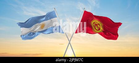 Gekreuzte Nationalflaggen der argentinischen und kirgisischen Flagge, die bei bewölktem Himmel im Wind winken. Symbolisieren von Beziehung, Dialog, Reisen zwischen zwei Ländern Stockfoto