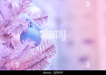 Teil eines rosa Weihnachtsbaums. Verziert mit blauen Kugeln auf Tannenzweigen mit verschwommenem Hintergrund. Hochwertige Fotos Stockfoto