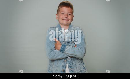 Fröhlich gut aussehend glücklich Kleinkind Junge in Jeans Jacke lächelnd, Blick auf die Kamera. Junge Mode Modell Teenager Kind Schüler indoor Studio Schuss isoliert auf grauem Hintergrund. Schönheit der männlichen Natur Stockfoto