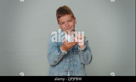 Ich brauche noch mehr, bitte gebt mir. Junge zeigt eine kleine Geste mit einem skeptischen Lächeln, zeigt ein minimales Zeichen, misst kleine Größe und bittet um Hilfe. Kinder Teenager Kind Kind auf grauem Studio Hintergrund Stockfoto